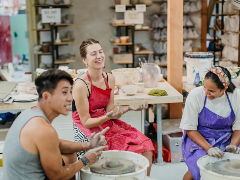 A group of adults smiling at a wheel throwing class